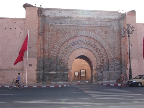 Carved stone gate Bab Agnaou in Marrakech, with red flag and cyclist