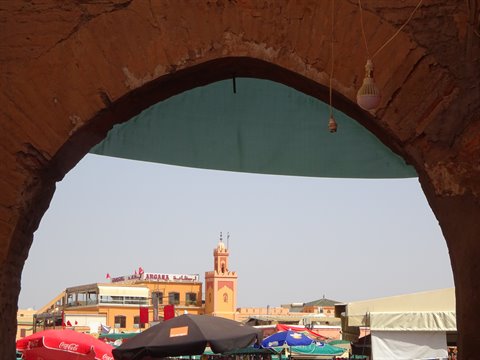 Red clay arch framing a minaret and market umbrellas, Marrakech