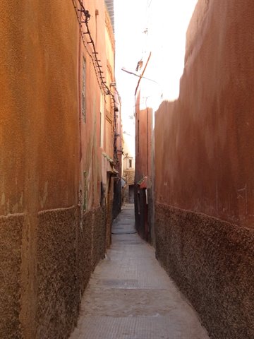 Narrow alley between ochre walls in Marrakech medina, bright light