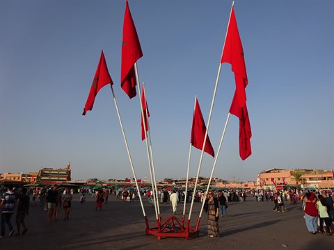 Red flags waving over Jemaa el-Fna square in Marrakech, crowds at dusk