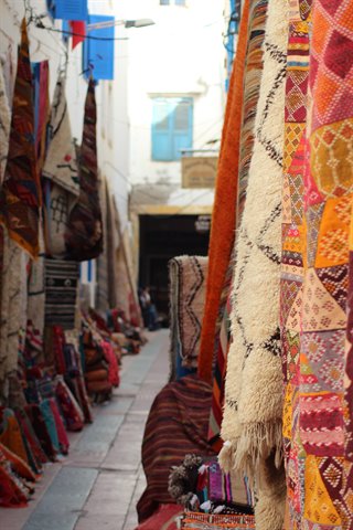Colorful Berber carpets hanging in a narrow medina alley, Essaouira