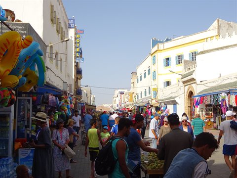 Busy street in Essaouira with souvenir stalls and white houses with blue shutters