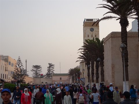 Crowd strolling the palm-lined avenue toward the clock tower, Essaouira