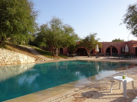 Blue pool among trees and earthen buildings in Skoura