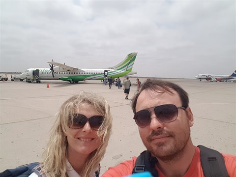 Couple selfie on Errachidia airport tarmac, parked green propeller plane