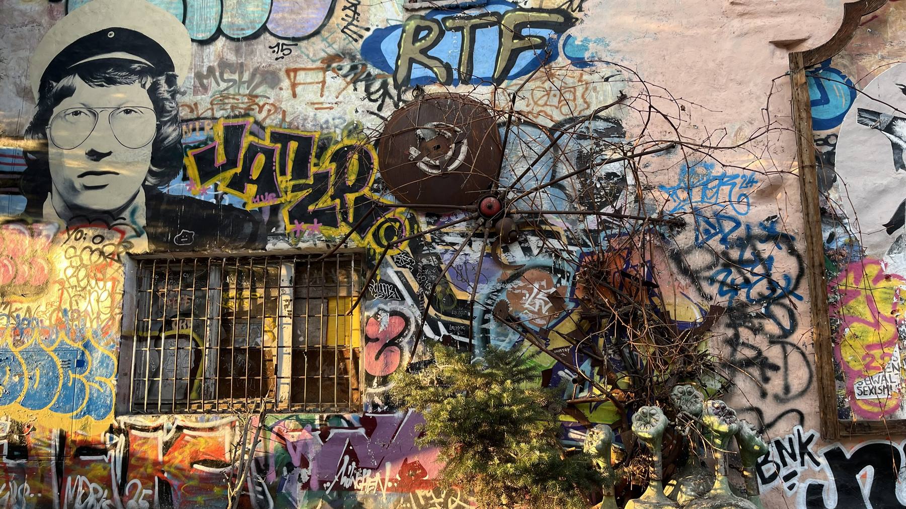Muro ricoperto di graffiti colorati, ritratto stencil, finestra sbarrata e rami secchi