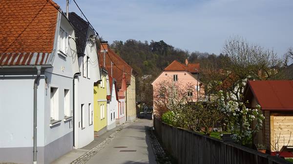 Alley with colorful houses, red roofs, wooden fence and wooded hill