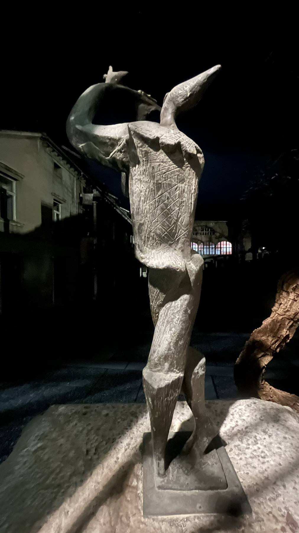 Scultura in pietra di figura con ali, illuminata di notte in strada urbana
