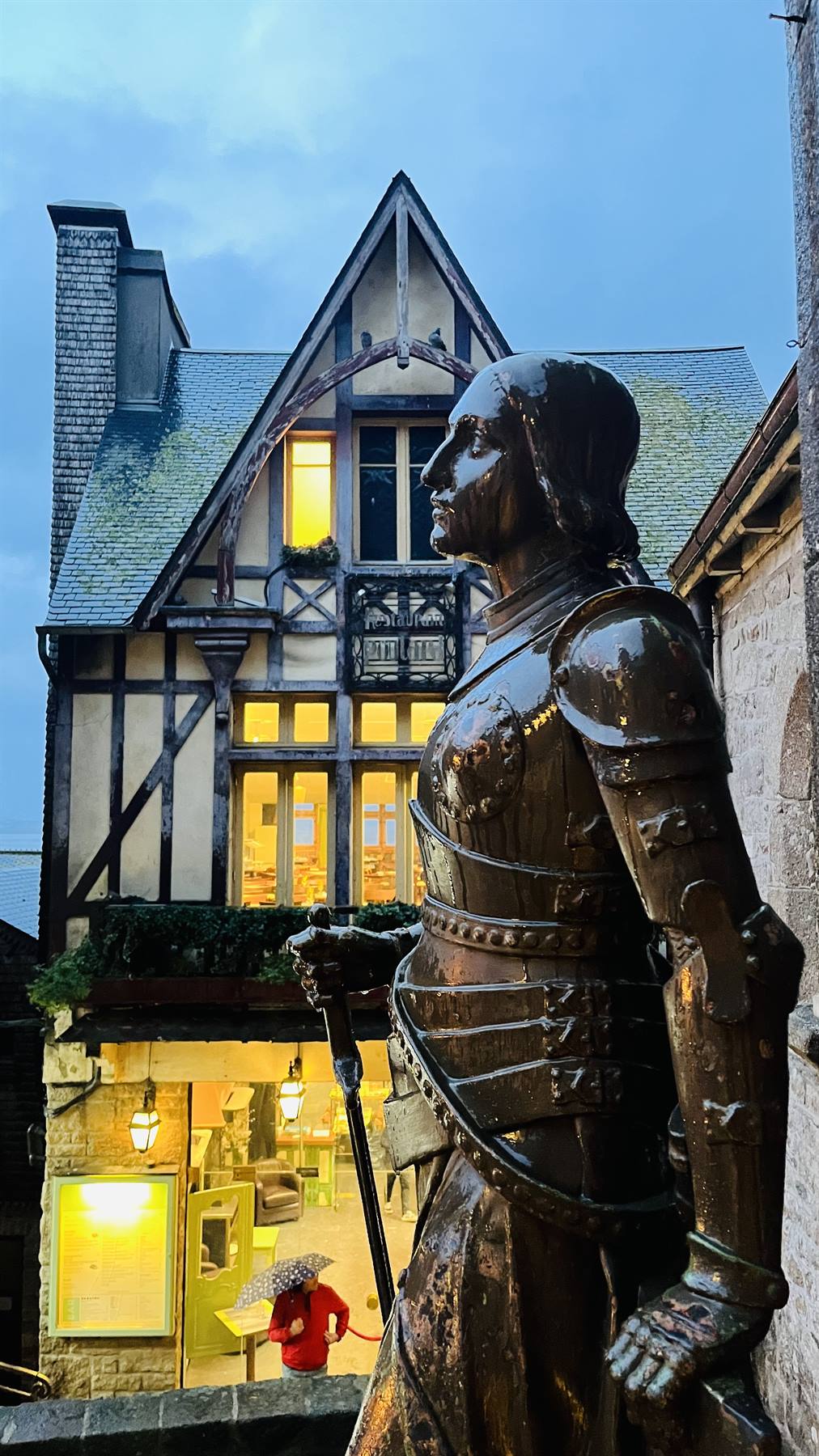 La statua veglia sul borgo antico mentre la pioggia accende le luci.