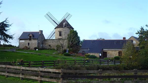 Old stone windmill with wooden sails among houses and grassy fences
