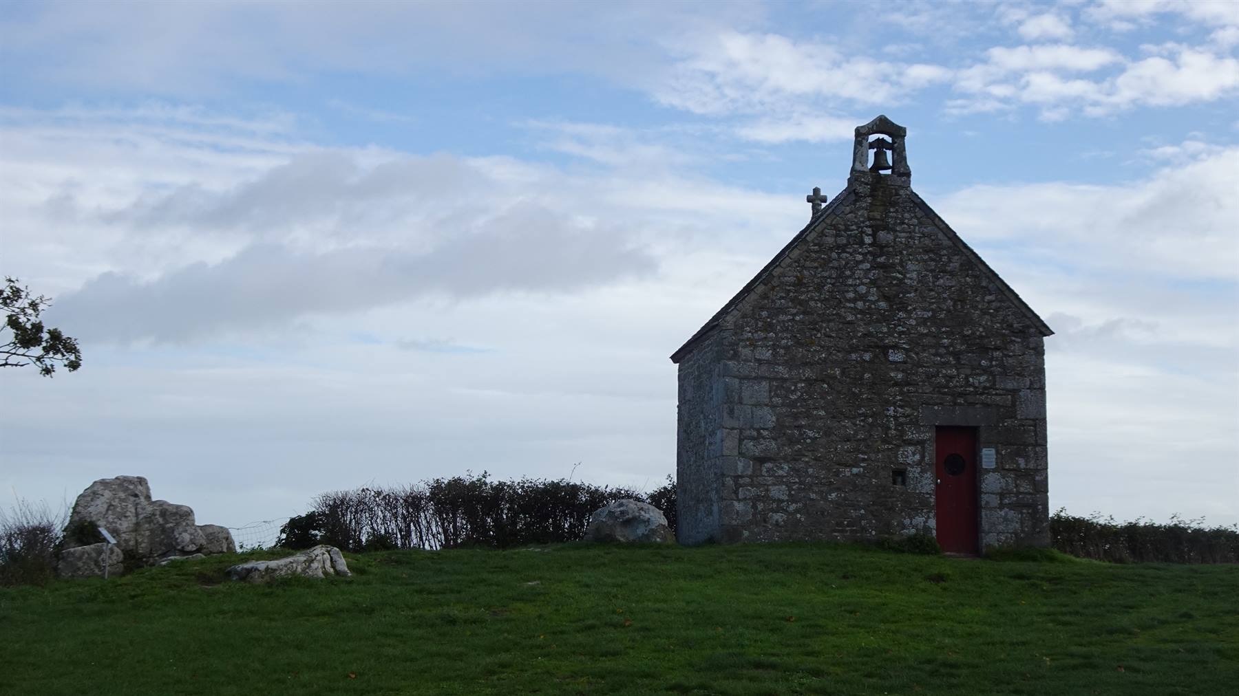 Cappella in pietra con campanile e porta rossa su collina erbosa