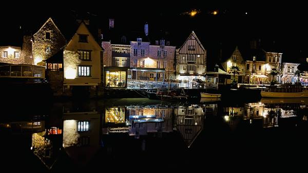 Timbered houses lit at night reflected in the harbor water of Auray