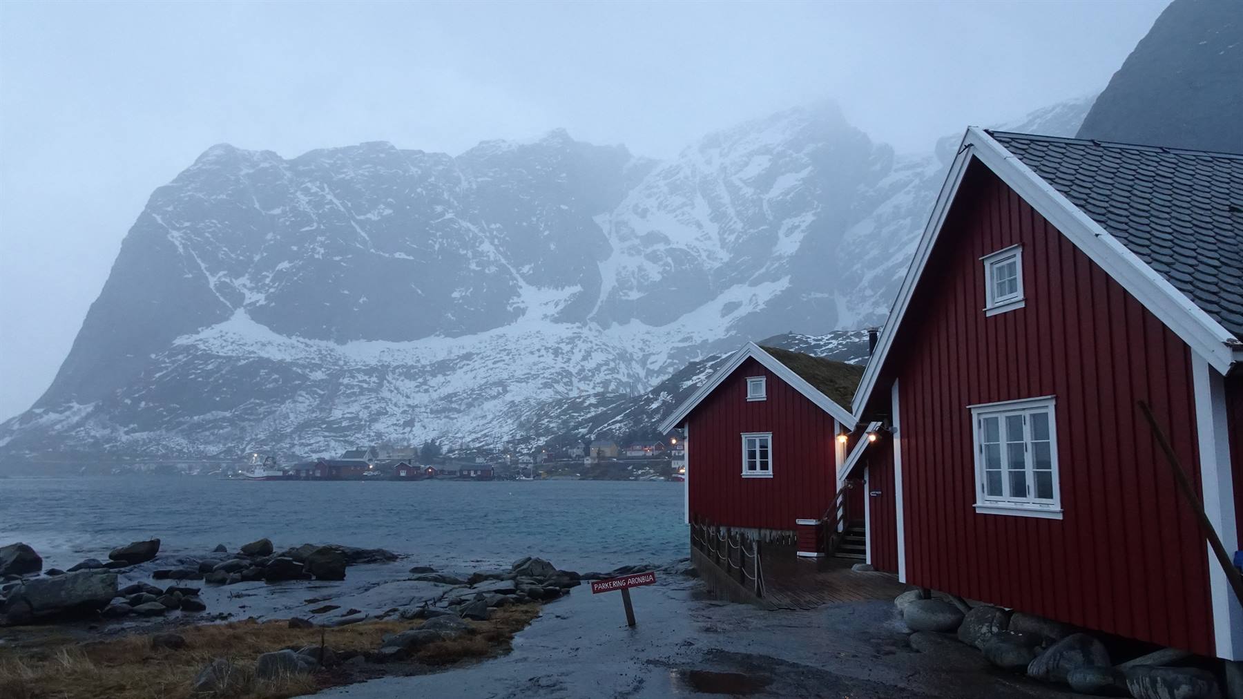 Casa rossa di legno sul mare, monti innevati nella nebbia, Lofoten