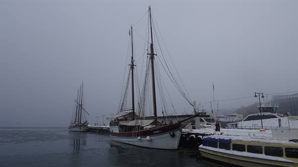 Wooden tall ship moored at the pier in fog, snow on ferry decks