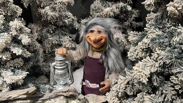 Troll figure with gray hair holding a lantern among snowy fir trees