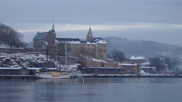 Snow-covered Akershus Fortress reflects in Oslo's grey harbour at dusk