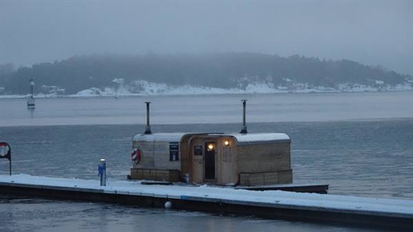 Wooden floating sauna glowing on snowy pier, icy sea and fog
