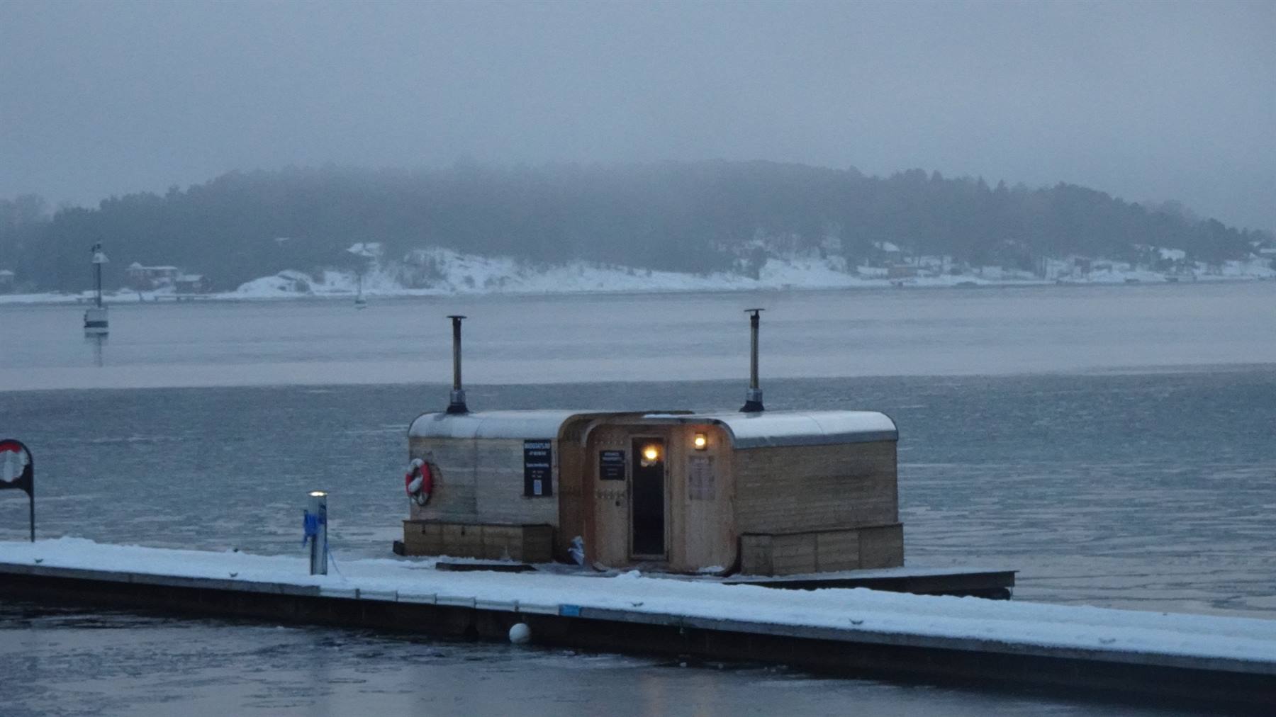 Sauna galleggiante in legno illuminata sul molo innevato, mare ghiacciato