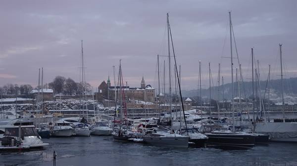 Sailboats moored in icy harbor, snow-covered fortress in background, Oslo