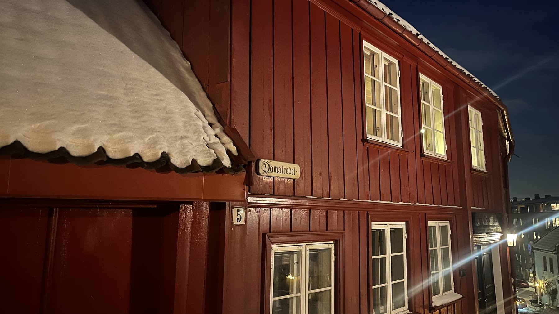 Red wooden house with snowy roof, Domkirkevegen sign, illuminated at night