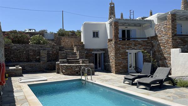 Blue pool with loungers in front of stone and whitewashed houses, Cyclades