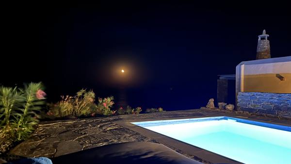 Lit swimming pool at night under the moon, stone terrace with flowers