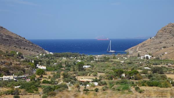 Green valley between dry hills, white houses and a sailboat on blue sea