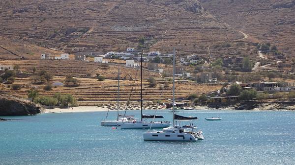 Catamarans and sailboats anchored in turquoise bay beneath arid hills with white houses