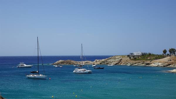 Sailboats and yachts anchored in turquoise bay, rocky shore and white houses under blue sky