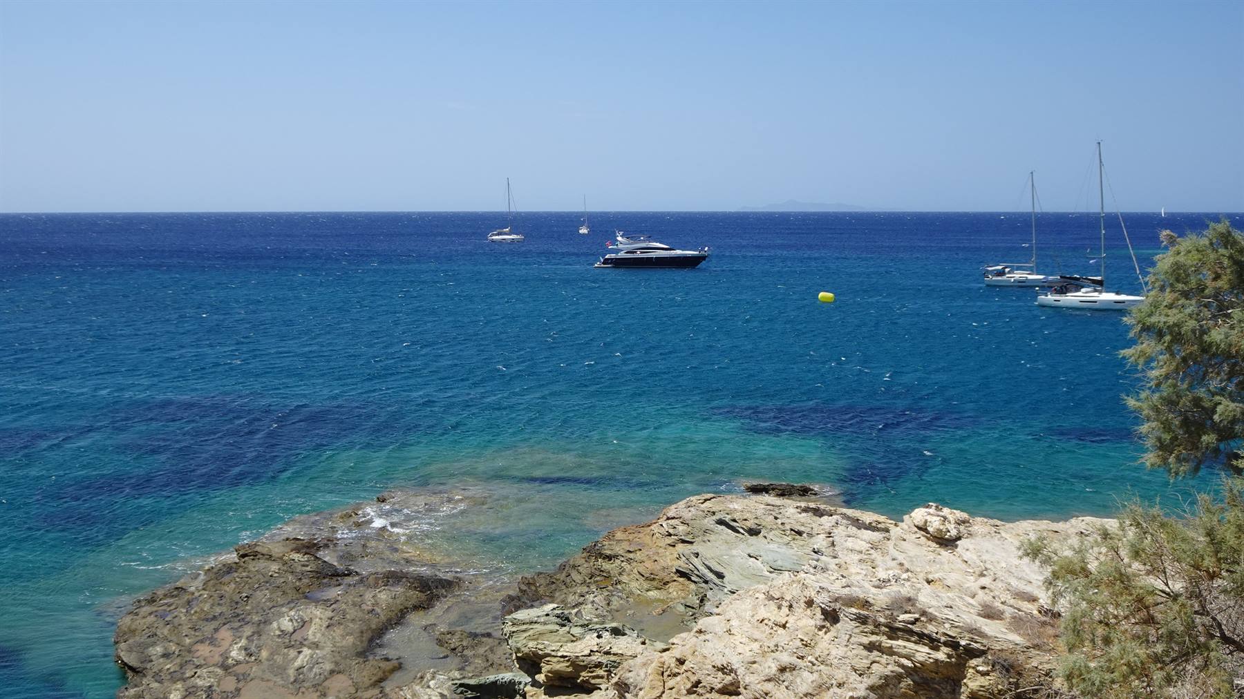 Barche a vela e yacht ancorati su mare turchese davanti a scoglichiari