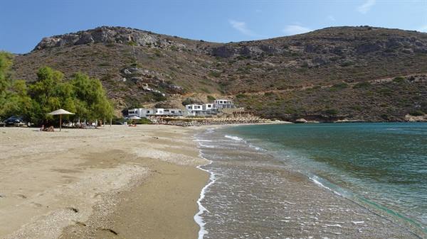 Clear waves on golden sand, white buildings beneath dry hills