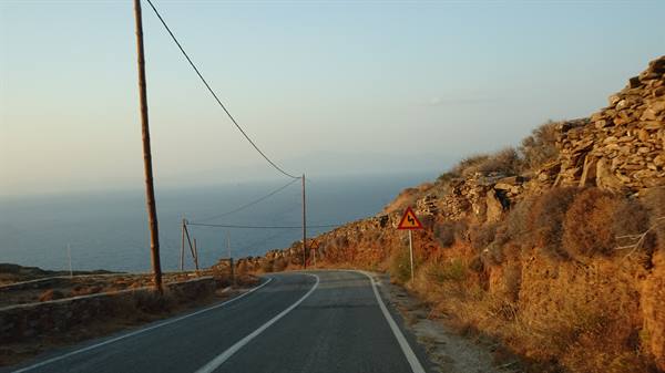 Asphalt road toward the sea beside stone walls and dry bushes in golden light