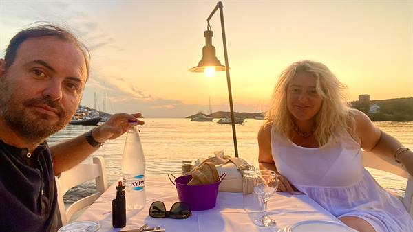 Couple at harbor taverna table with water bottle and boats at sunset