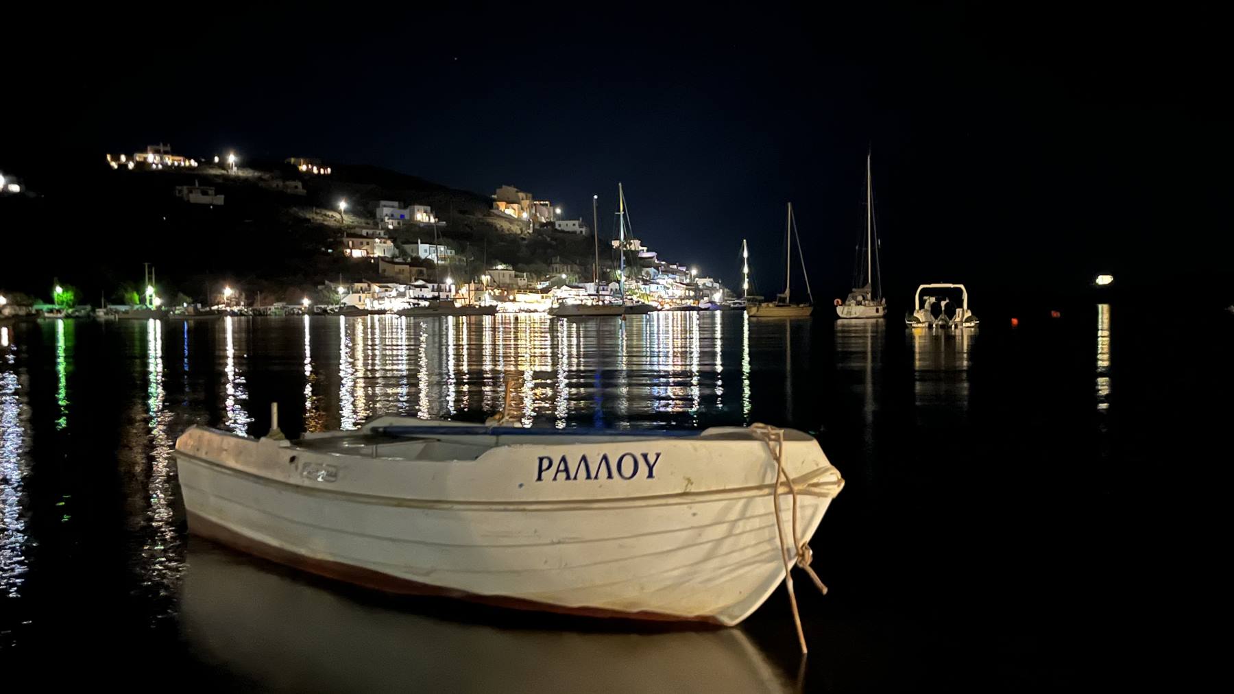 Barca bianca in legno in primo piano, porto illuminato di notte sullo sfondo