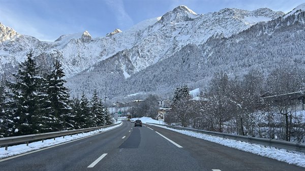 Snowy road toward Chamonix, cars between firs and snow-capped peaks