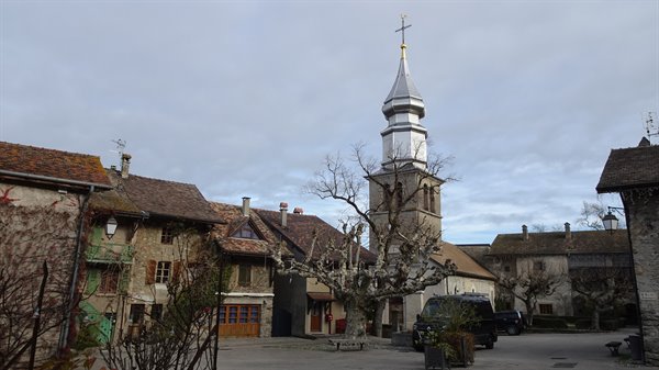 Silver church spire of Yvoire among old stone houses under cloudy sky