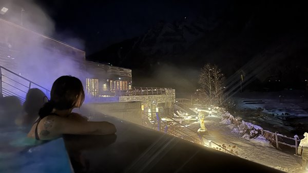 Woman relaxing in outdoor heated pool at night, steam and snowy peaks, Chamonix