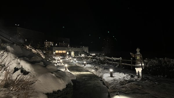Snowy path at night with glowing lamps, statues and lit chalets in Chamonix