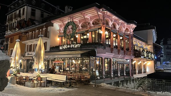 Illuminated pink wooden restaurant at night, snow and empty terrace chairs, Chamonix