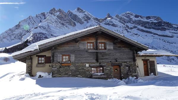Wooden and stone chalet in snow beneath the Col des Aravis mountains