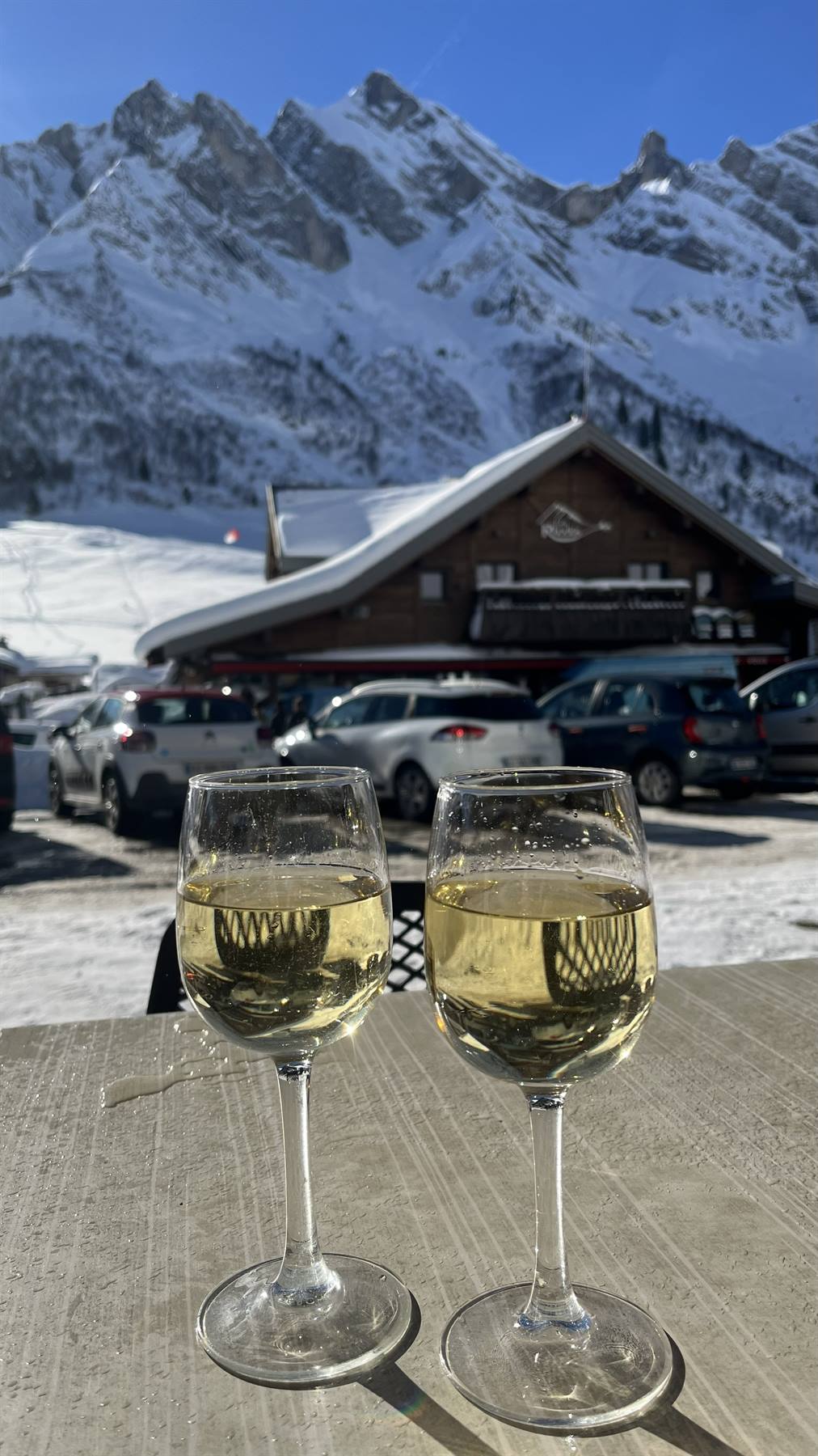 Due calici di vino bianco su tavolo in pietra, chalet innevato e montagne a Col des Aravis