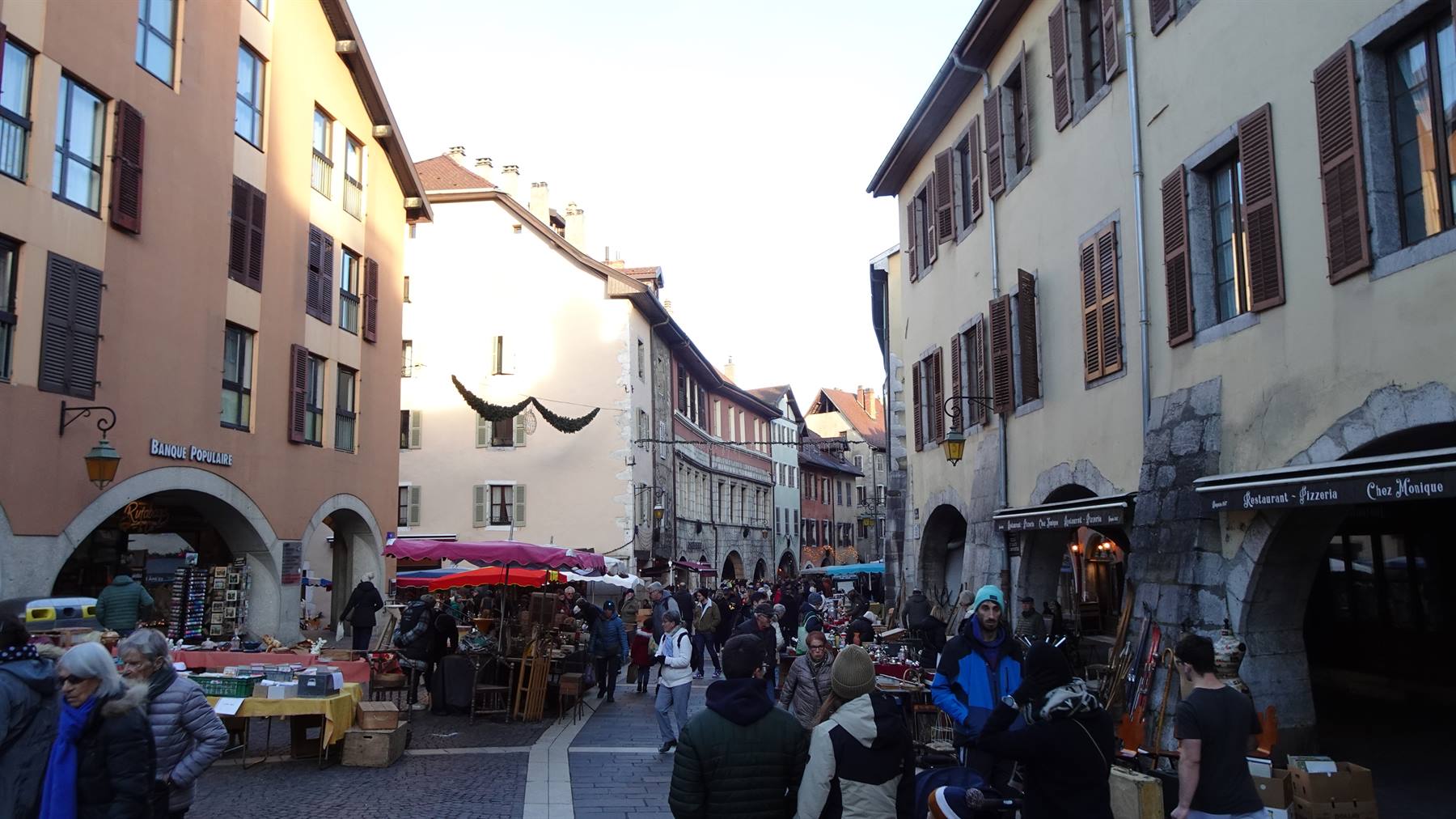 Mercato in piazza ad Annecy, case antiche con archi e passaanti tra i banchi