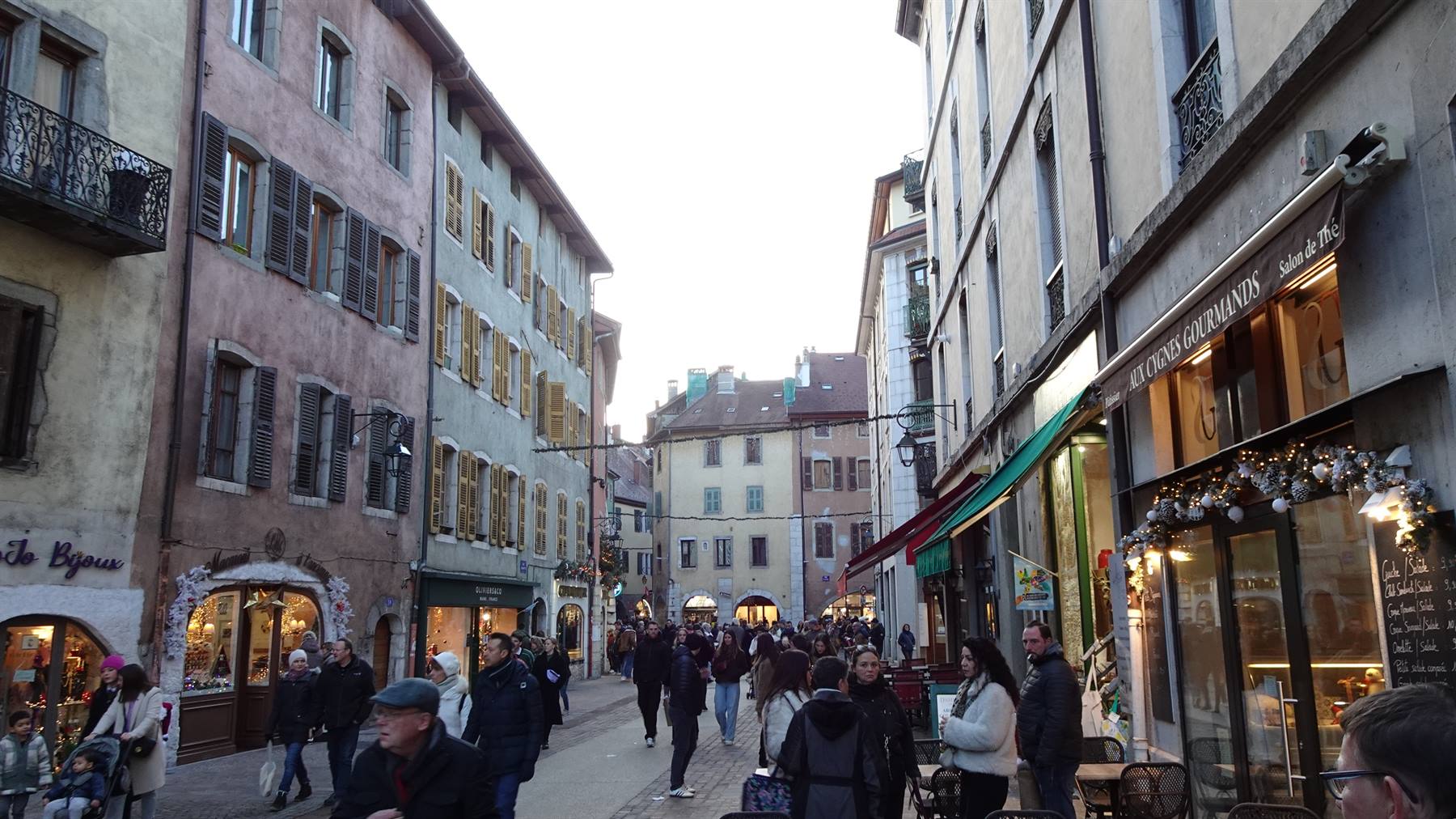 Via pedonale affollata tra case antiche colorate con negozi, Annecy