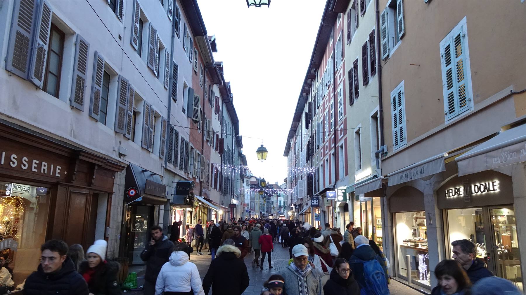 Via pedonale affollata di Annecy, case colorate con persiane e luci natalizie
