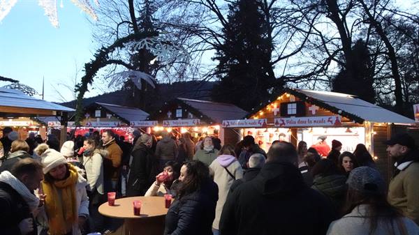 Christmas market in Annecy, visitors with mulled wine cups among lit wooden chalets
