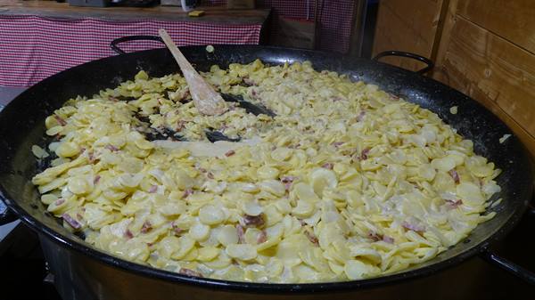 Giant pan of tartiflette: potatoes, bacon and melted cheese stirred with a wooden spoon