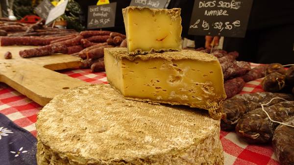 Cheeses and sausages on market stall with red checkered cloth, price chalkboard