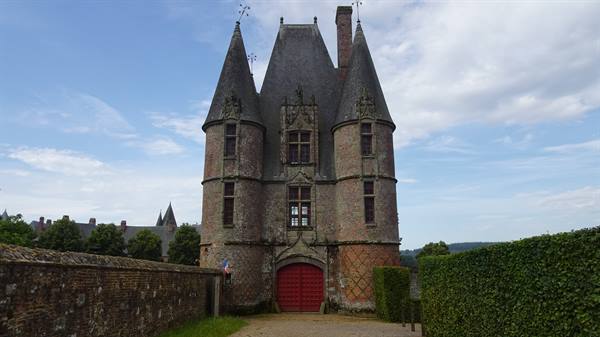 Brick castle with conical towers and red gate among hedges