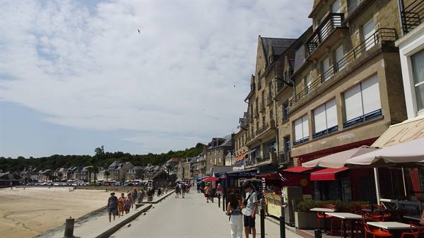 Cancale seafront, stone buildings, red restaurant umbrellas, people strolling along the promenade