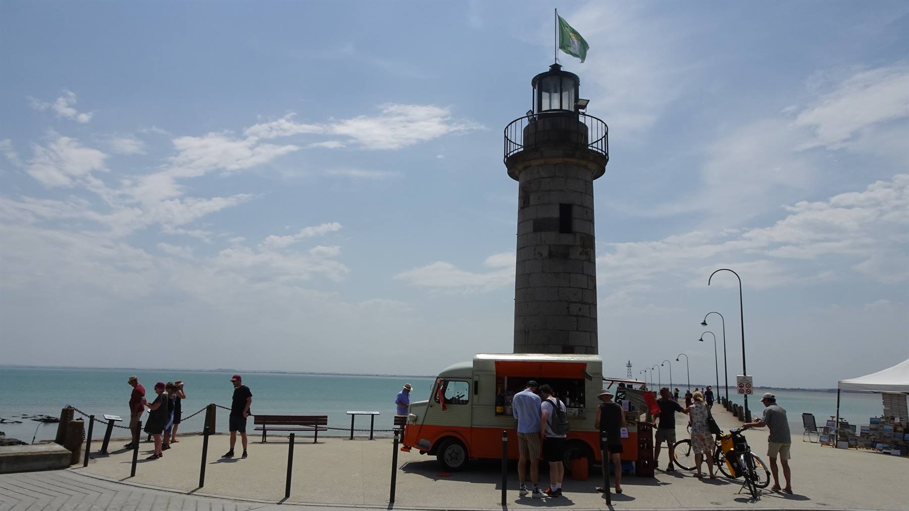 Turisti attorno a un furgone food sotto il faro in pietra sul molo di Cancale